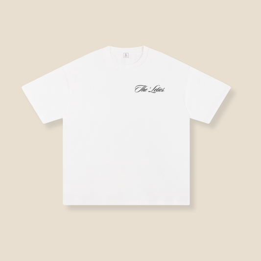 White t-shirt with 'The Leleis' logo on a beige background