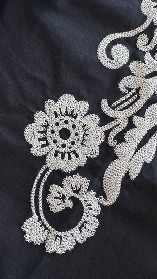 Close-up of a black fabric garment featuring intricate silver floral and scroll embroidery.