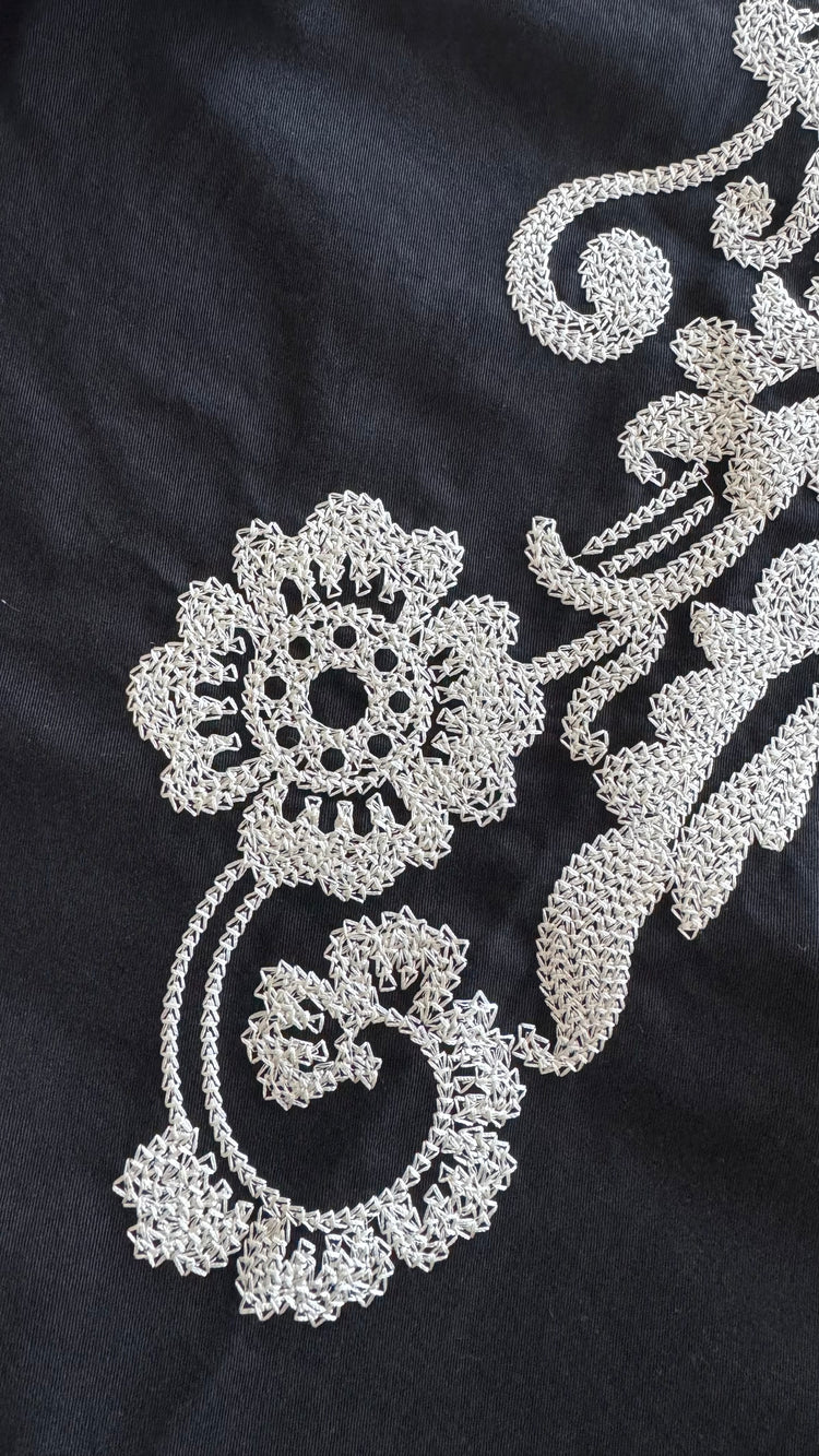 Close-up of a black fabric garment featuring intricate silver floral and scroll embroidery.