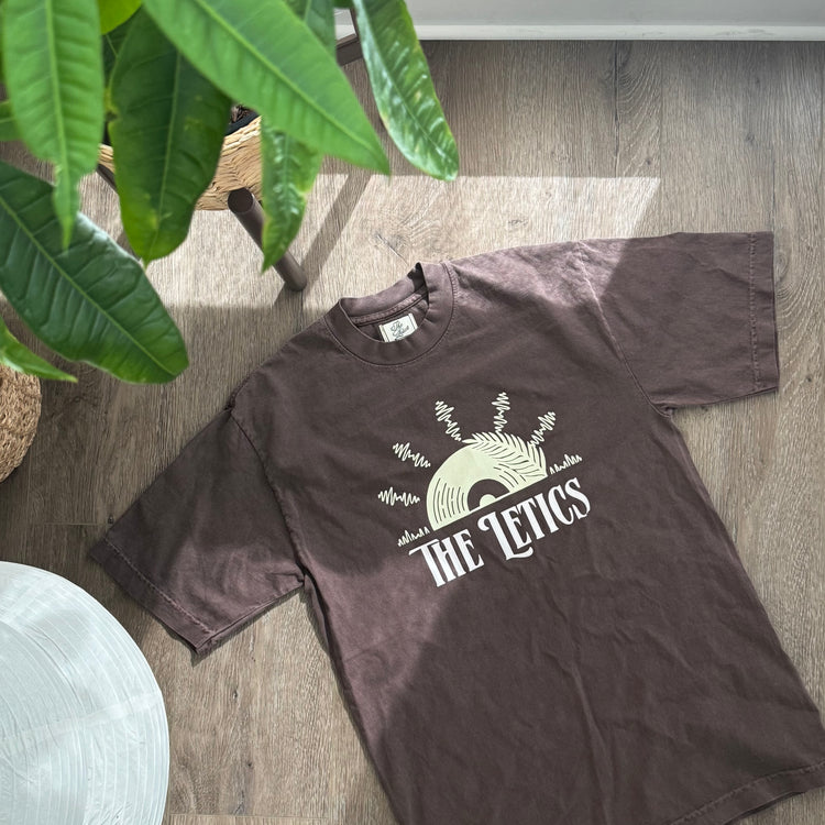 Brown t-shirt with "The 'Letics" white puff print logo and screen pressed vinyl/sun/palm tree yellow design above logo in shape of sunset.
