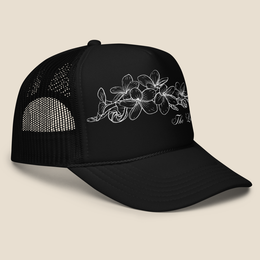 Black foam trucker hat with embroidered Champei, or also known as Plumeria flower, side view.